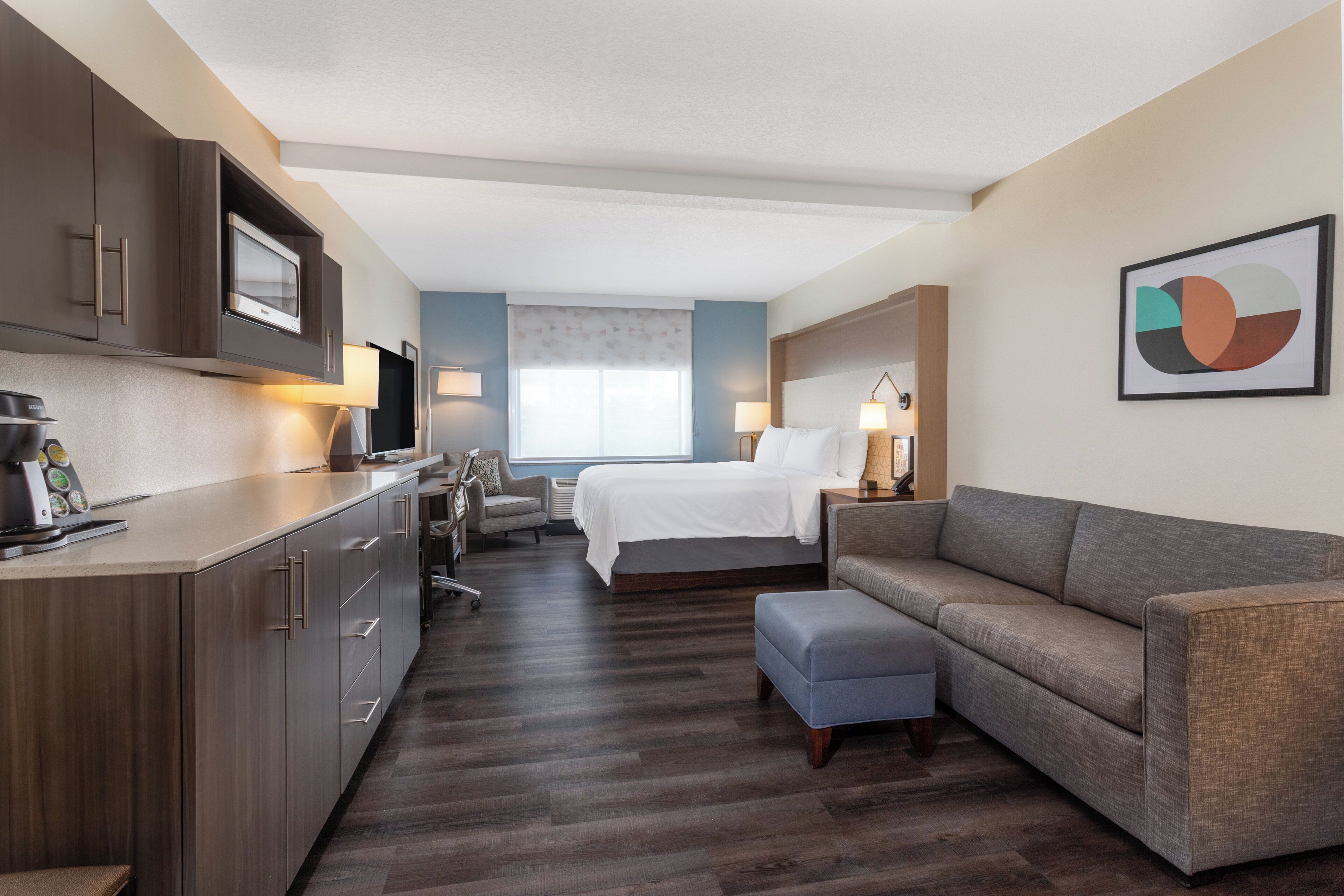 Ein Hotelzimmer mit einer Küchenzeile, einem Bett, einem Schlafsofa und einem Schreibtisch.