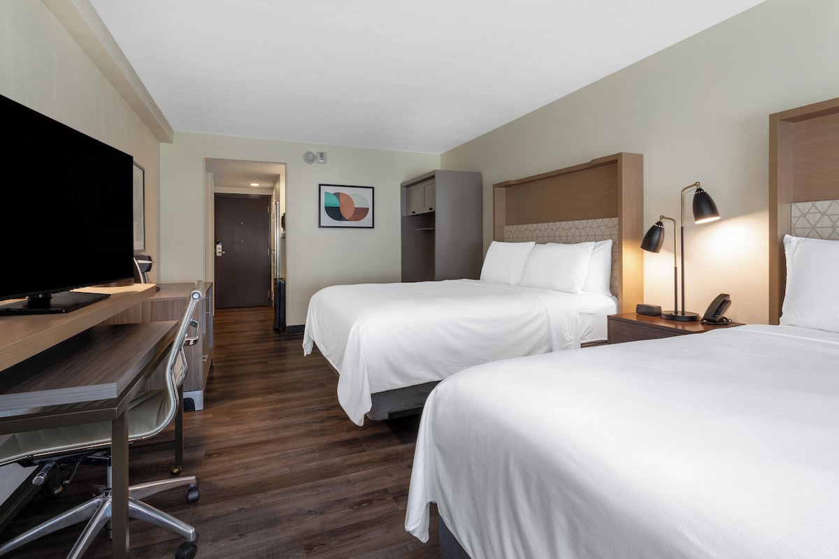 A hotel room with two beds, a desk with a TV, and a coat rack.