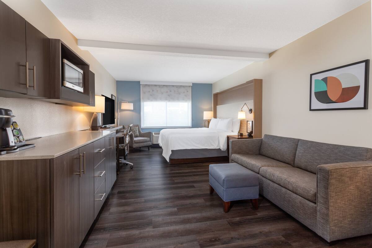 A hotel room with a kitchenette, a bed, a sofa, and a desk.