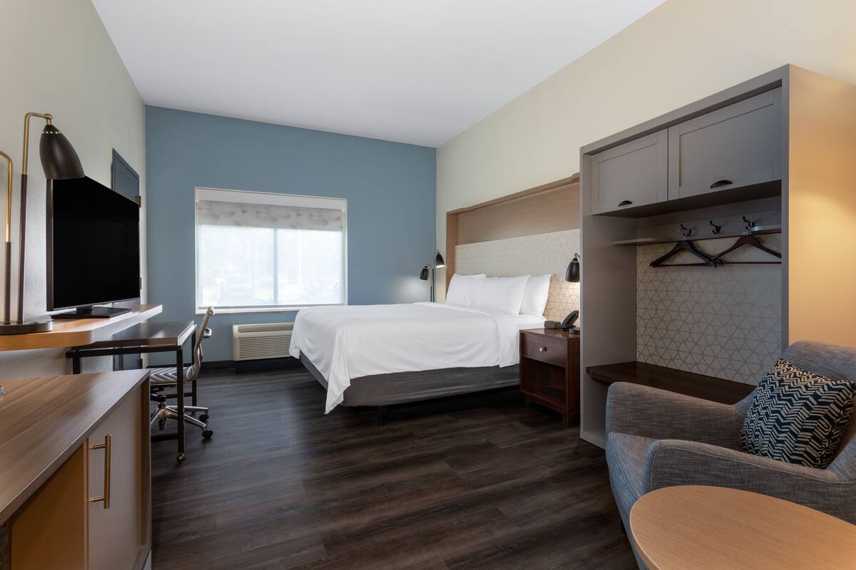 A hotel room with a bed, a desk with a TV, a chair, a sofa, and a wardrobe.
