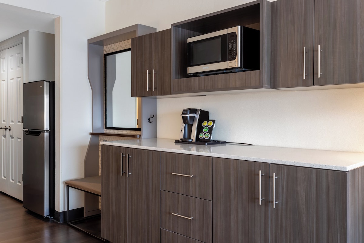 A modern kitchen with dark wood cabinets, a stainless steel refrigerator, a microwave, and a coffee maker.