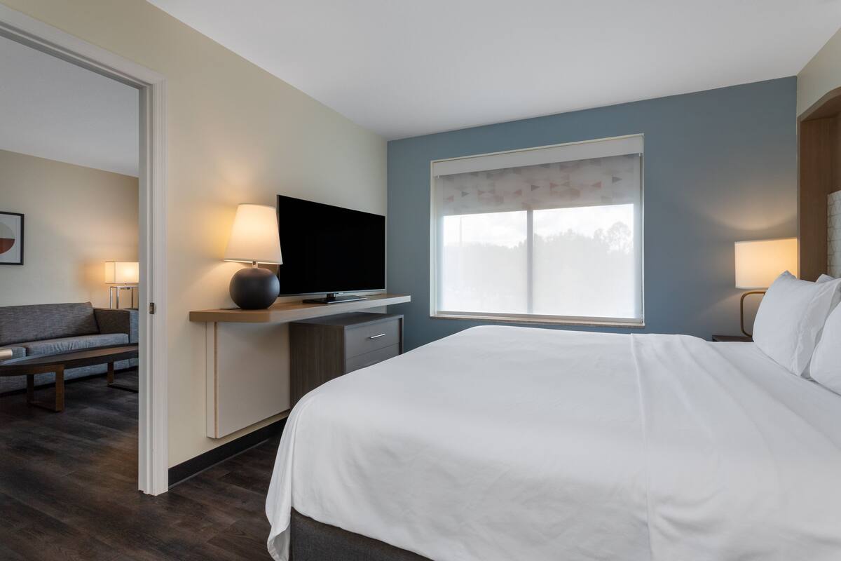 A hotel room with a bed, a desk with a flat-screen TV, a sofa, and a window with a view.