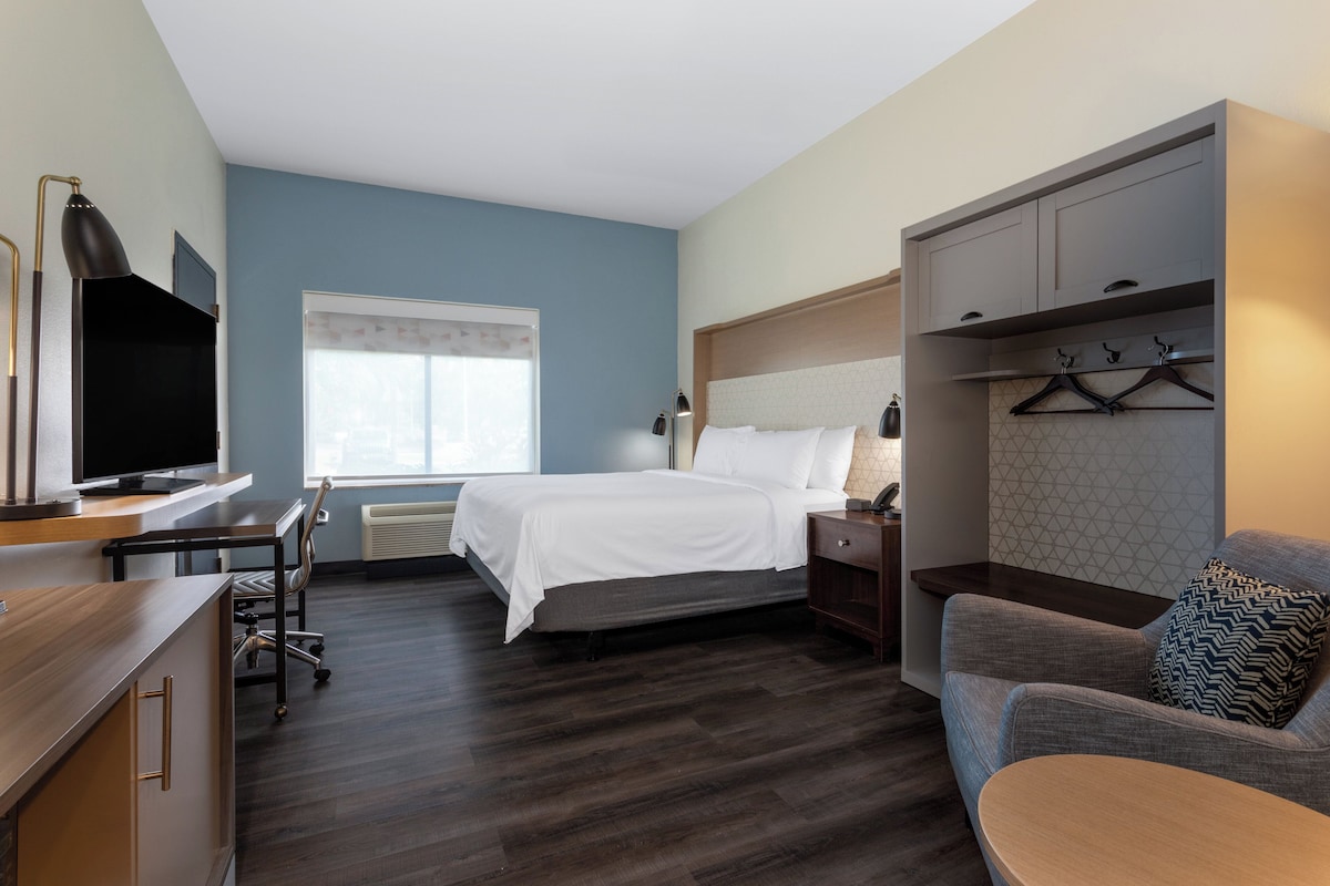 A hotel room with a bed, a desk with a TV, a chair, a sofa, and a wardrobe.