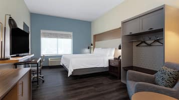 Habitación de hotel con cama, escritorio con televisor, una silla, un sofá y un armario con perchas.