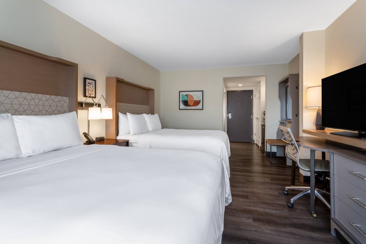 A hotel room with two beds, a desk with a chair, a television, and a painting on the wall.