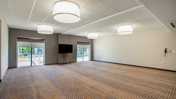 A spacious room with a patterned carpet, large windows, and three ceiling lights.