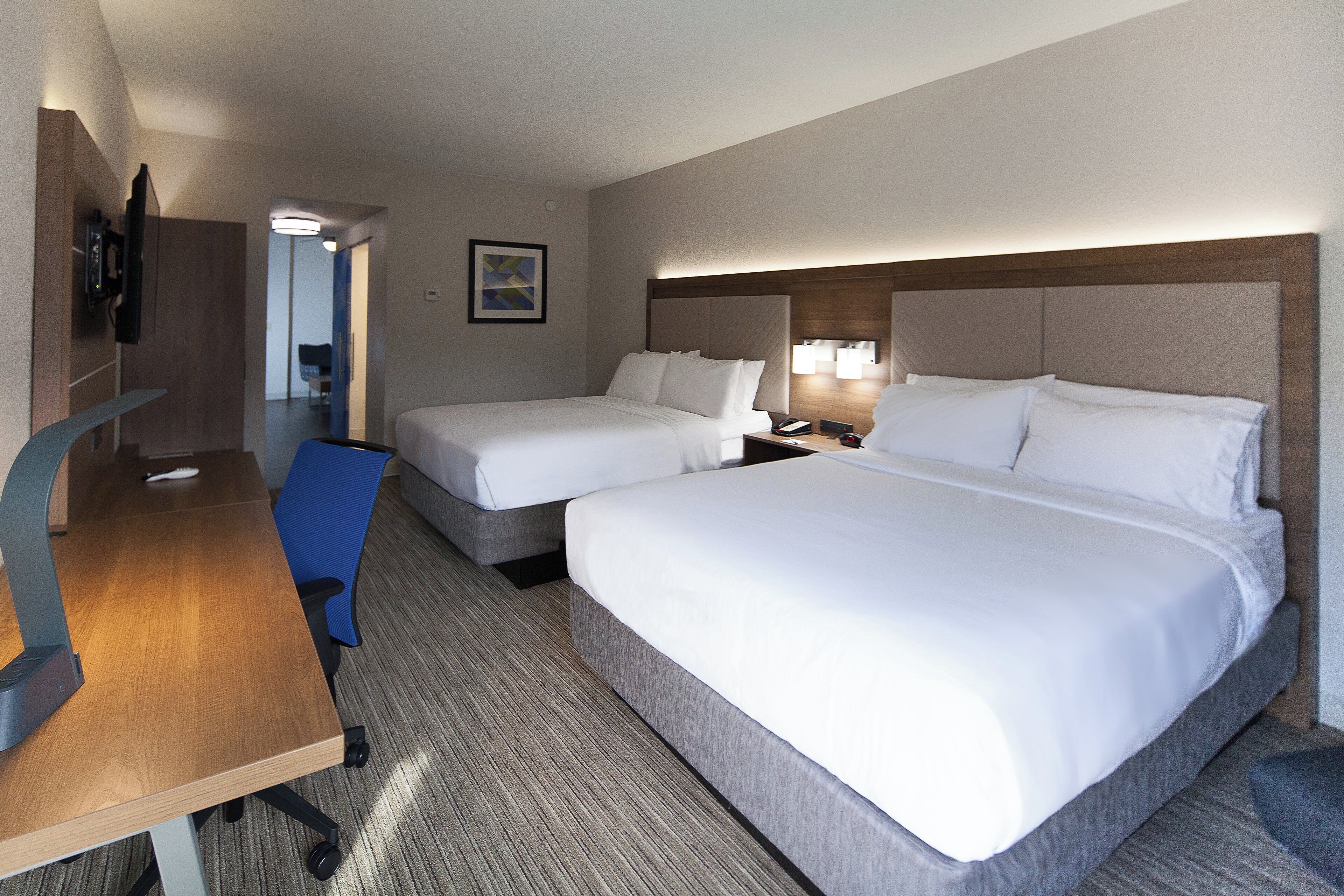 A hotel room with two beds, a desk, a chair, and a TV.