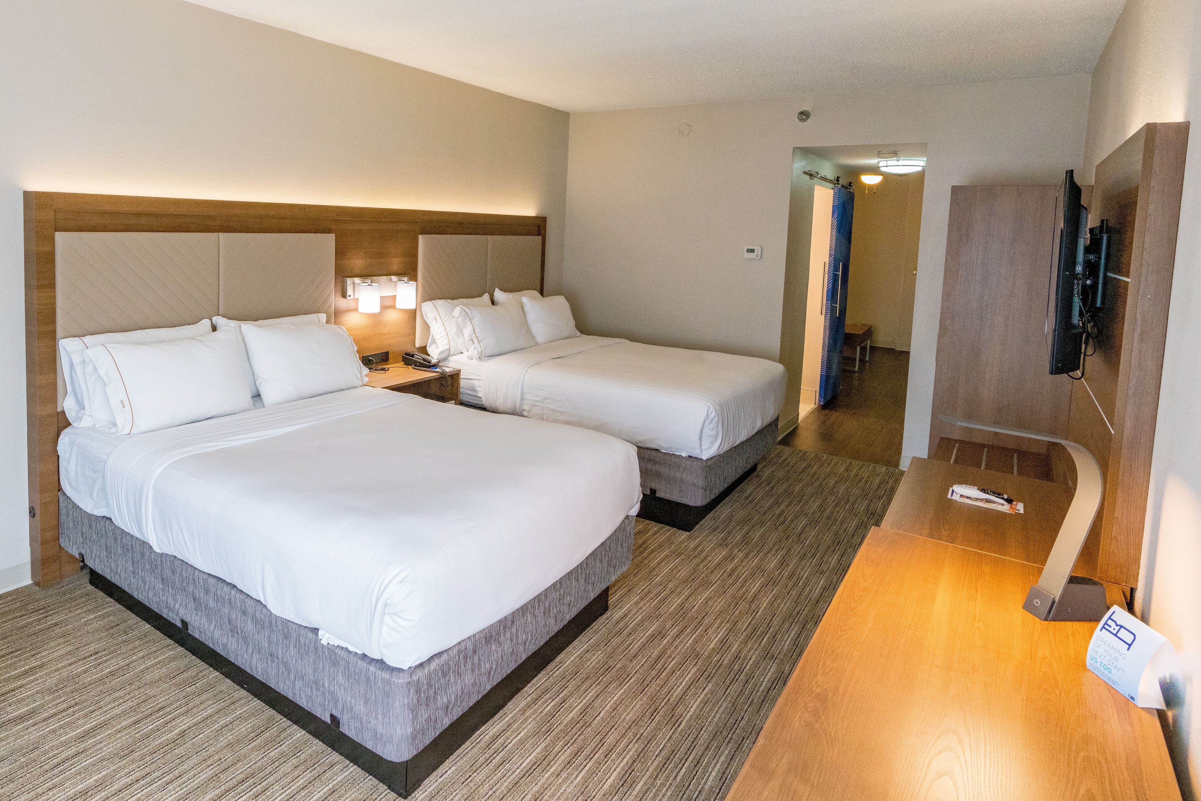 Habitación de hotel con dos camas, un escritorio, un televisor y un baño a la vista.