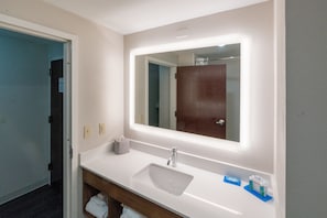 Une salle de bain avec un lavabo blanc, un miroir avec un éclairage intégré et un meuble-lavabo en bois.