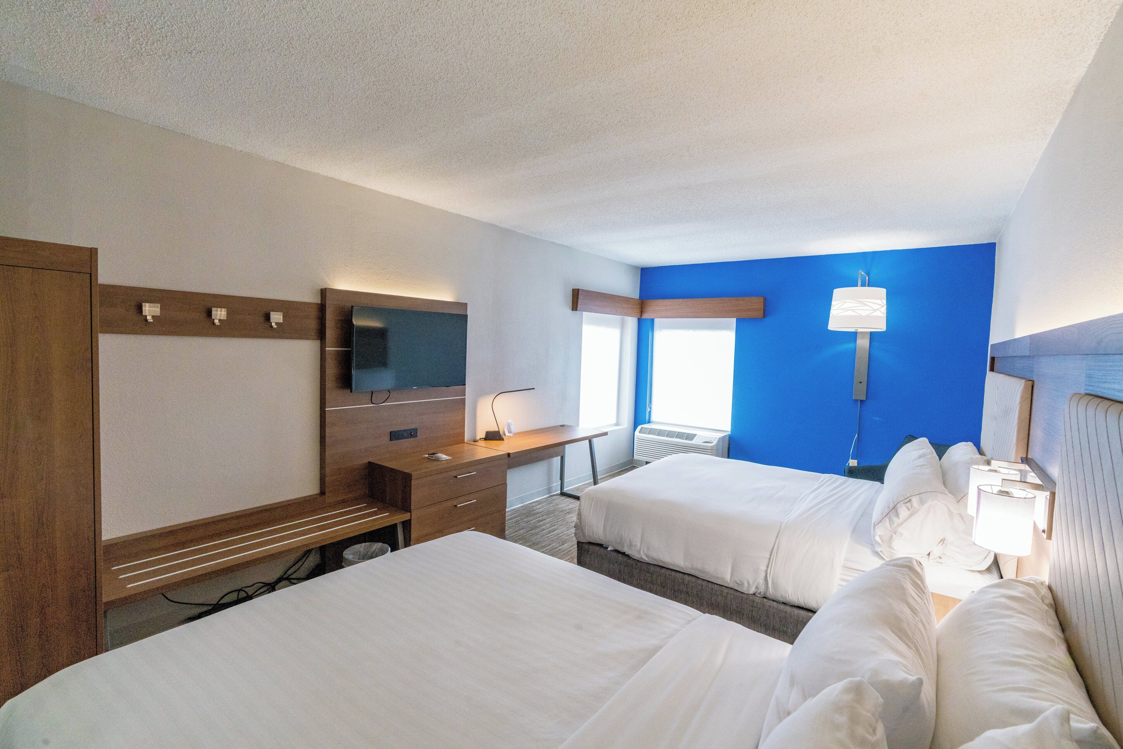 Une chambre d’hôtel avec deux lits, un bureau, une chaise, une télévision et une fenêtre.