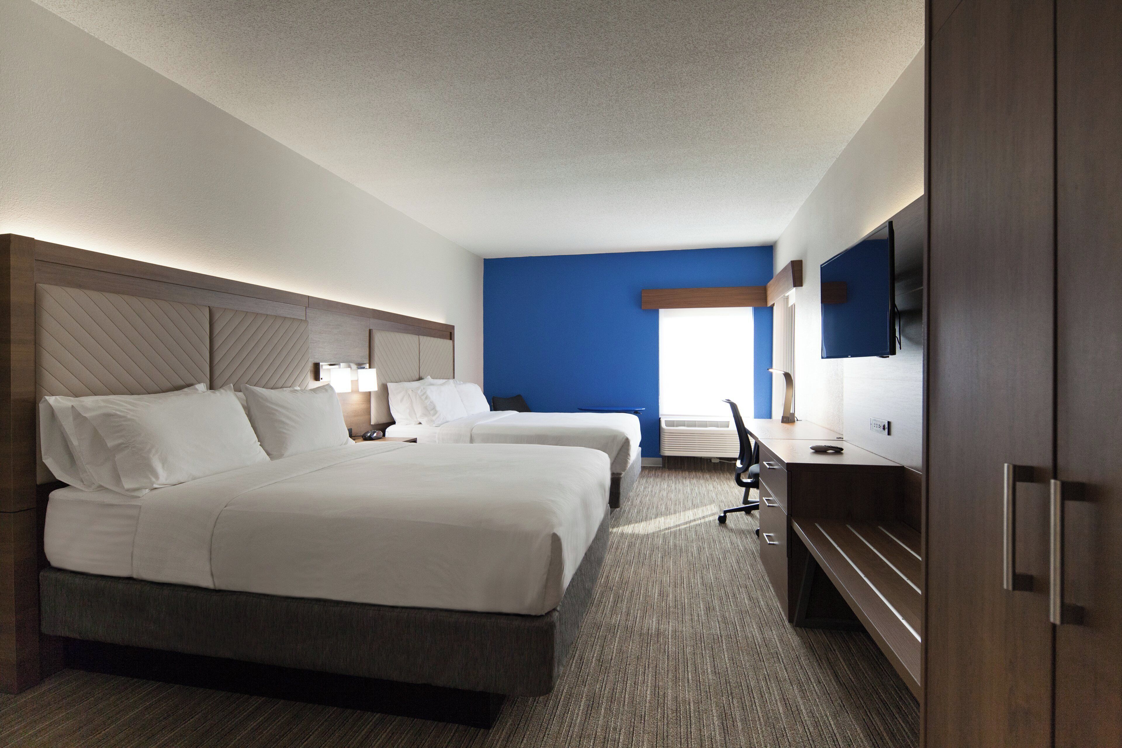 A hotel room with two beds, a desk, a flat-screen TV, and a window.