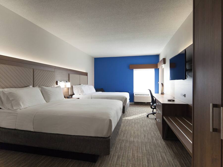 A hotel room with two beds, a desk, a flat-screen TV, and a window.