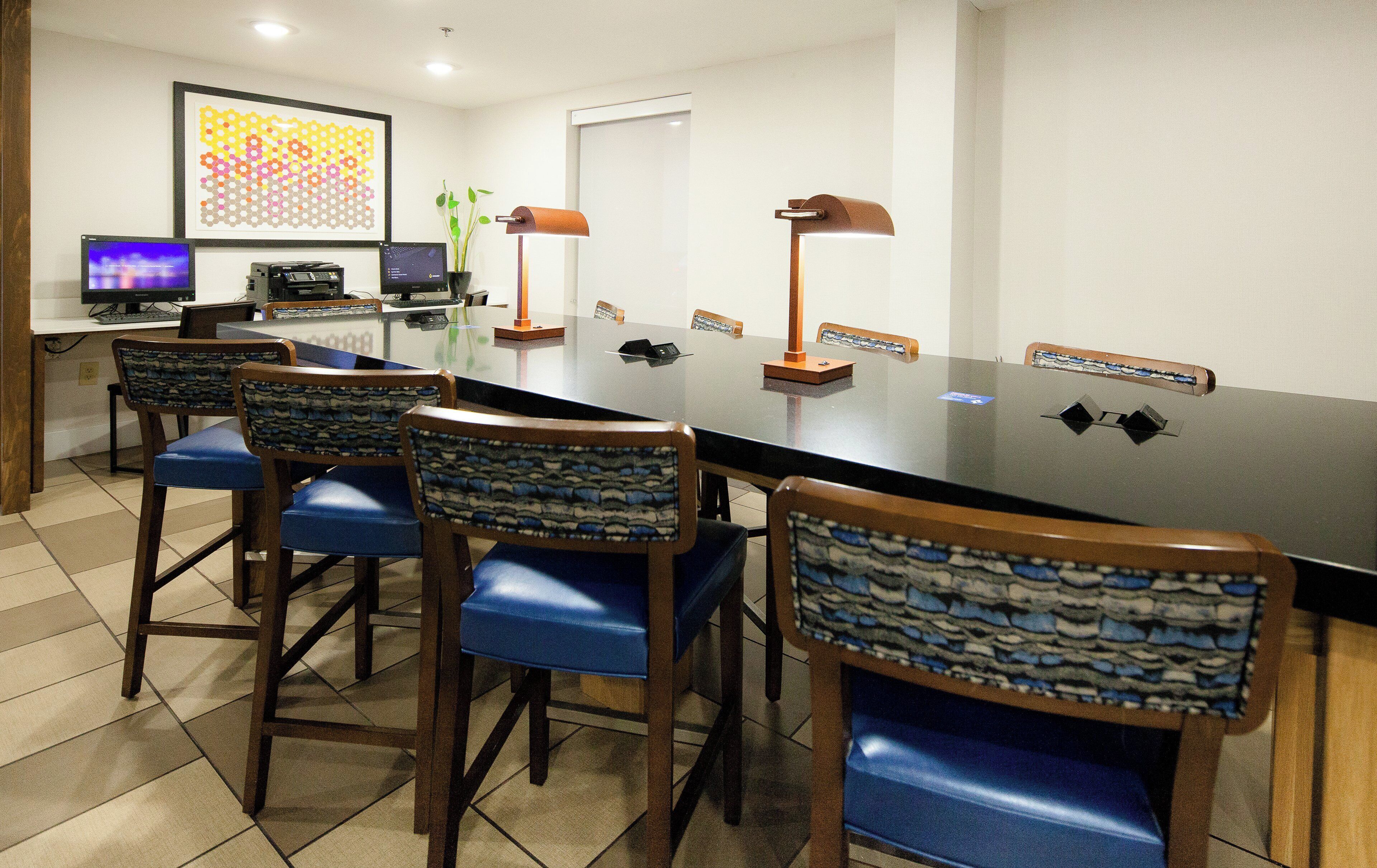 Une salle de conférence avec une longue table, des chaises, un ordinateur portable, un ordinateur de bureau et une œuvre d’art encadrée accrochée au mur.