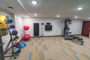 Une salle de sport équipée de matériel d’exercice, d’un téléviseur fixé au mur et d’un tapis à motifs.
