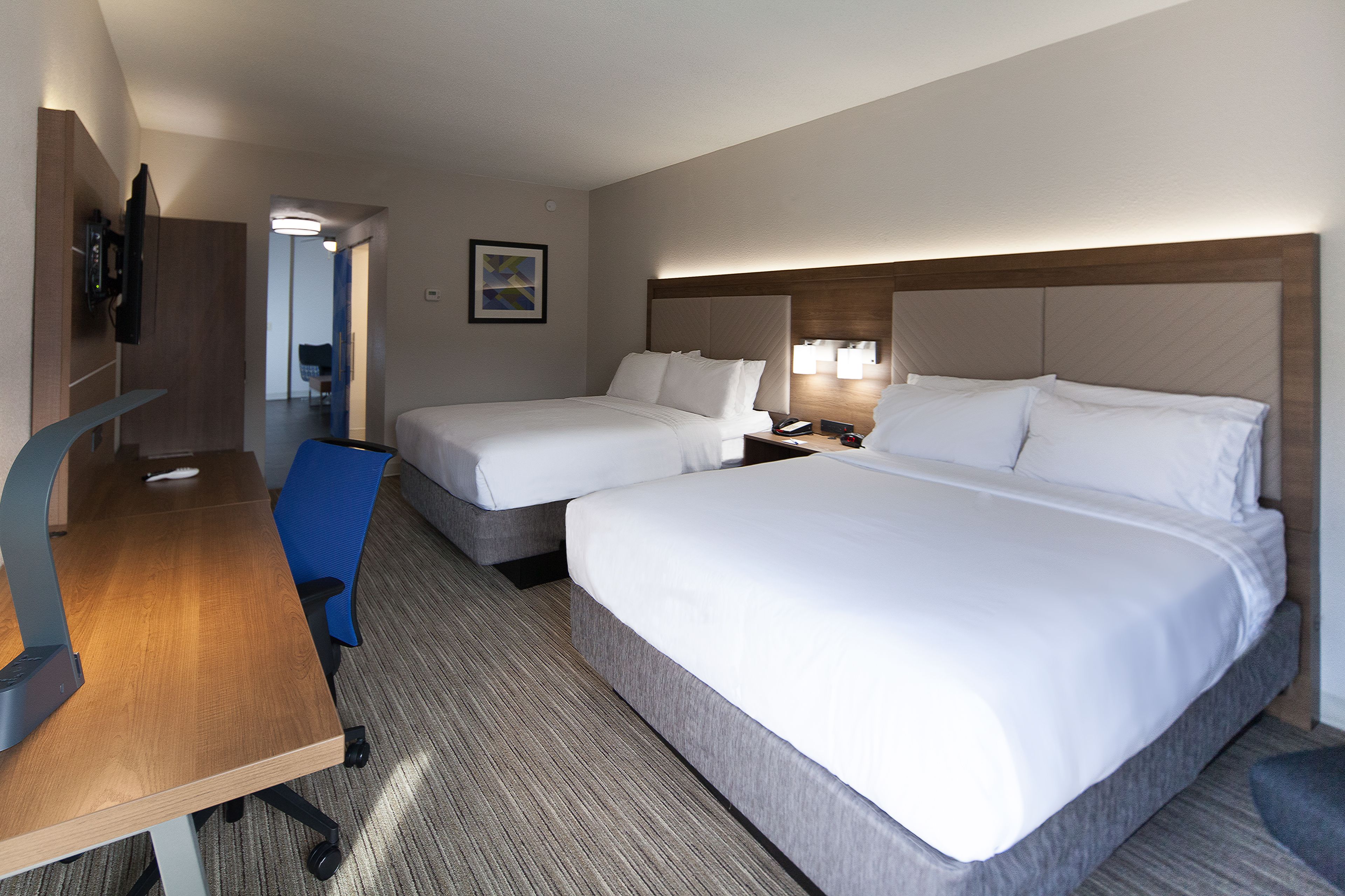 Ein Hotelzimmer mit zwei Einzelbetten, einem Schreibtisch mit Stuhl, einem Fernseher und einem durchgegangenen Badezimmer.