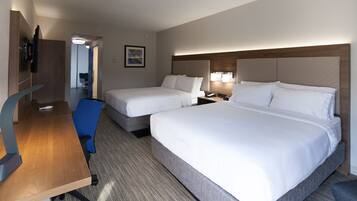 Habitación de hotel con dos camas individuales, un escritorio con silla, televisor y baño a la vista a través de una puerta abierta.