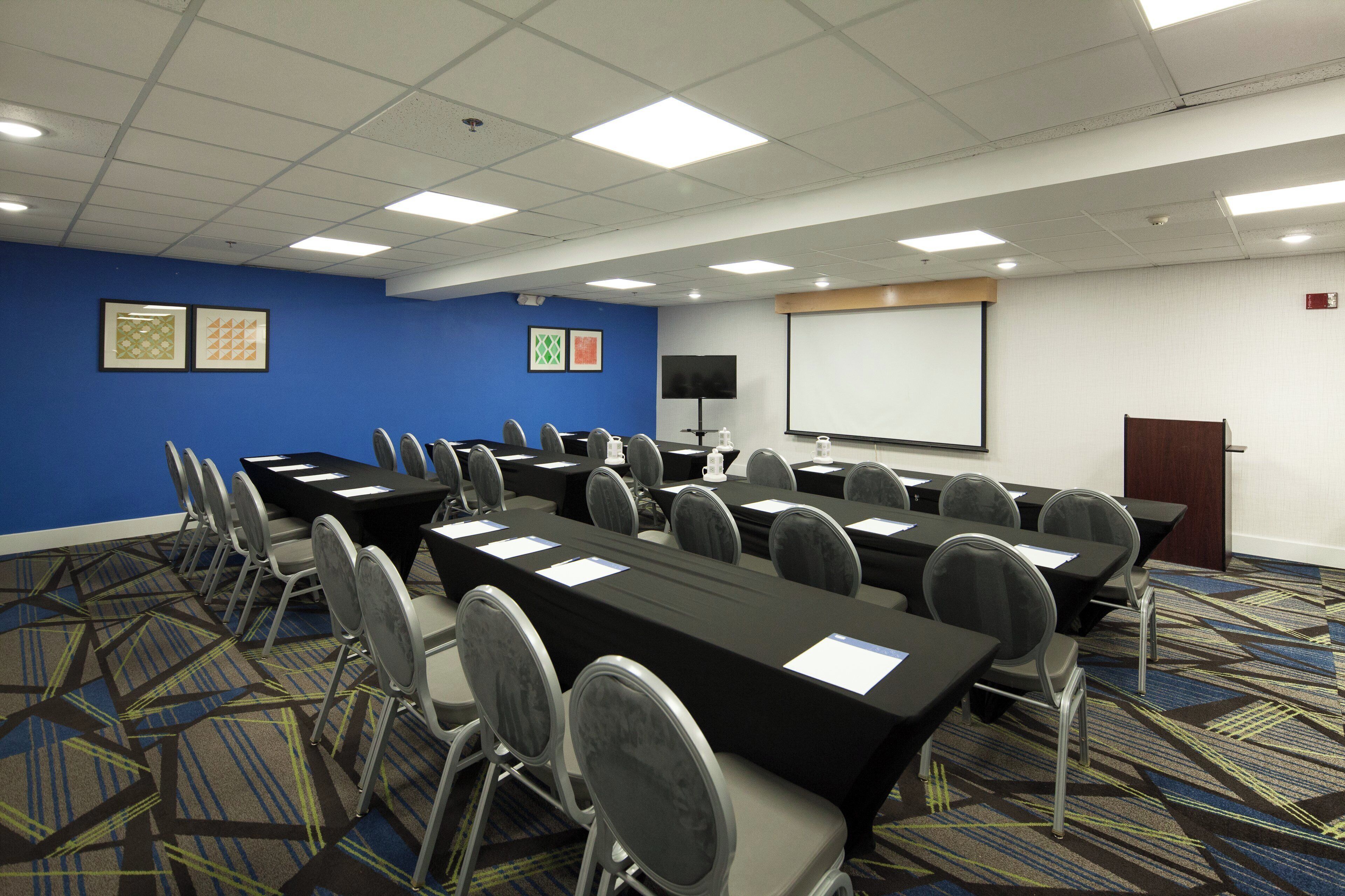 A conference room with tables, chairs, a projector screen, and a presentation screen.