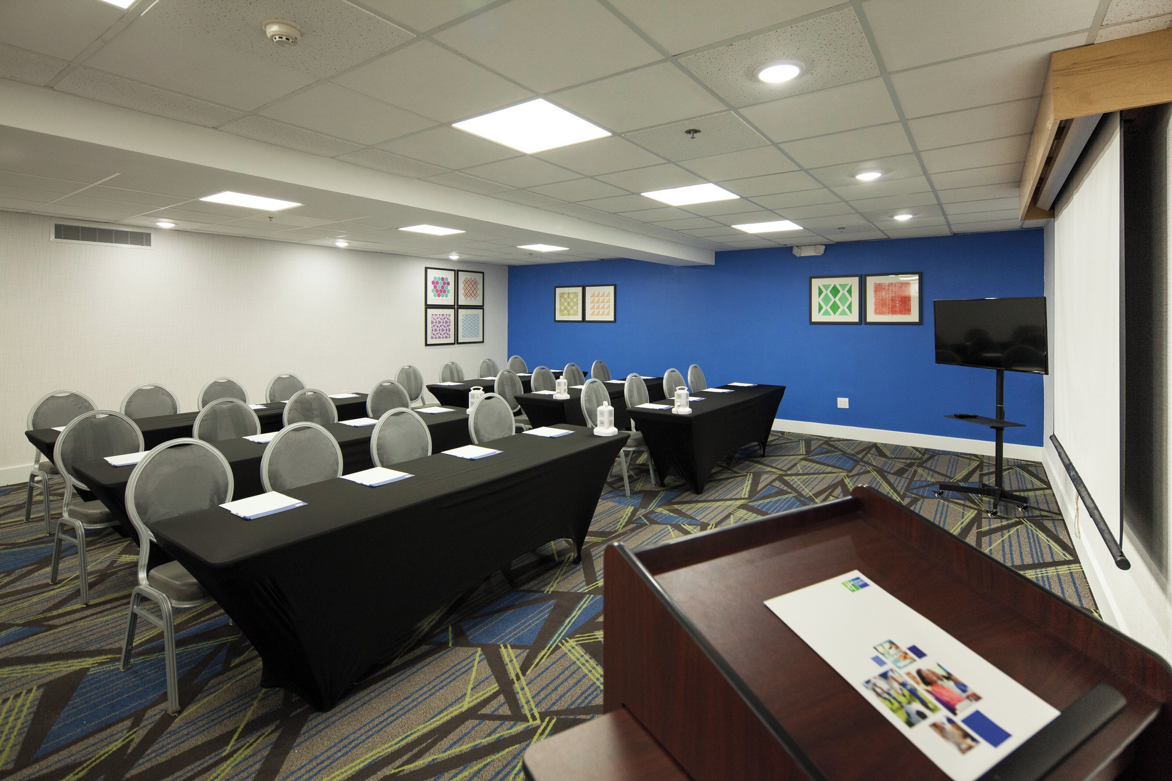 A conference room with a long table, chairs, a podium, and a television screen.
