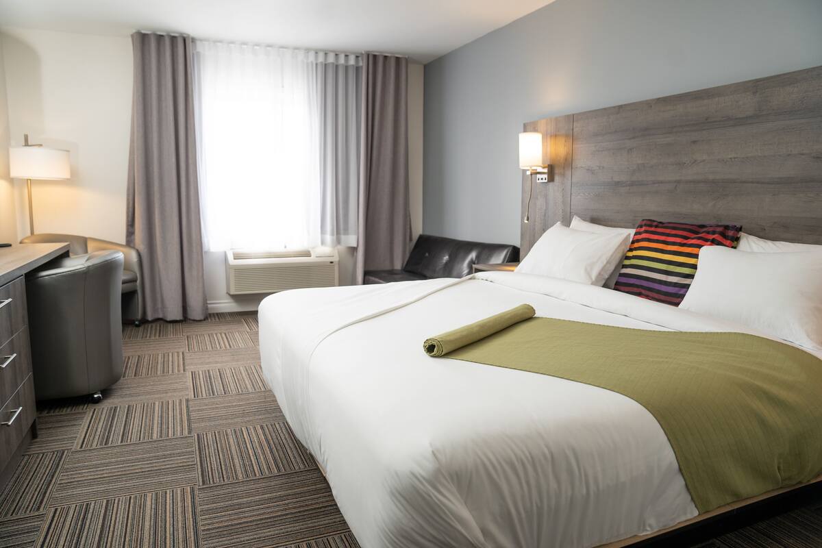 Une chambre d’hôtel avec un grand lit, un bureau, une chaise, une lampe et une fenêtre avec des rideaux.