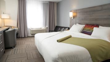 Una habitación de hotel con una cama grande, un escritorio, una silla, una lámpara y una ventana con cortinas.