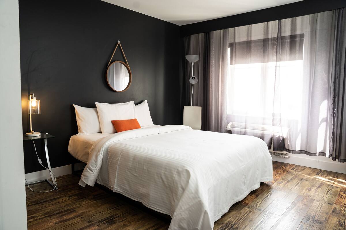 Une chambre d’hôtel moderne avec un grand lit, une table de chevet, une lampe et une fenêtre avec des rideaux.