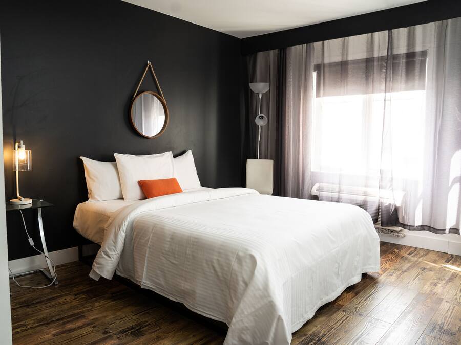 Ein modernes Hotelzimmer mit einem großen Bett, einem Nachttisch, einer Lampe und einem Fenster mit Vorhängen.