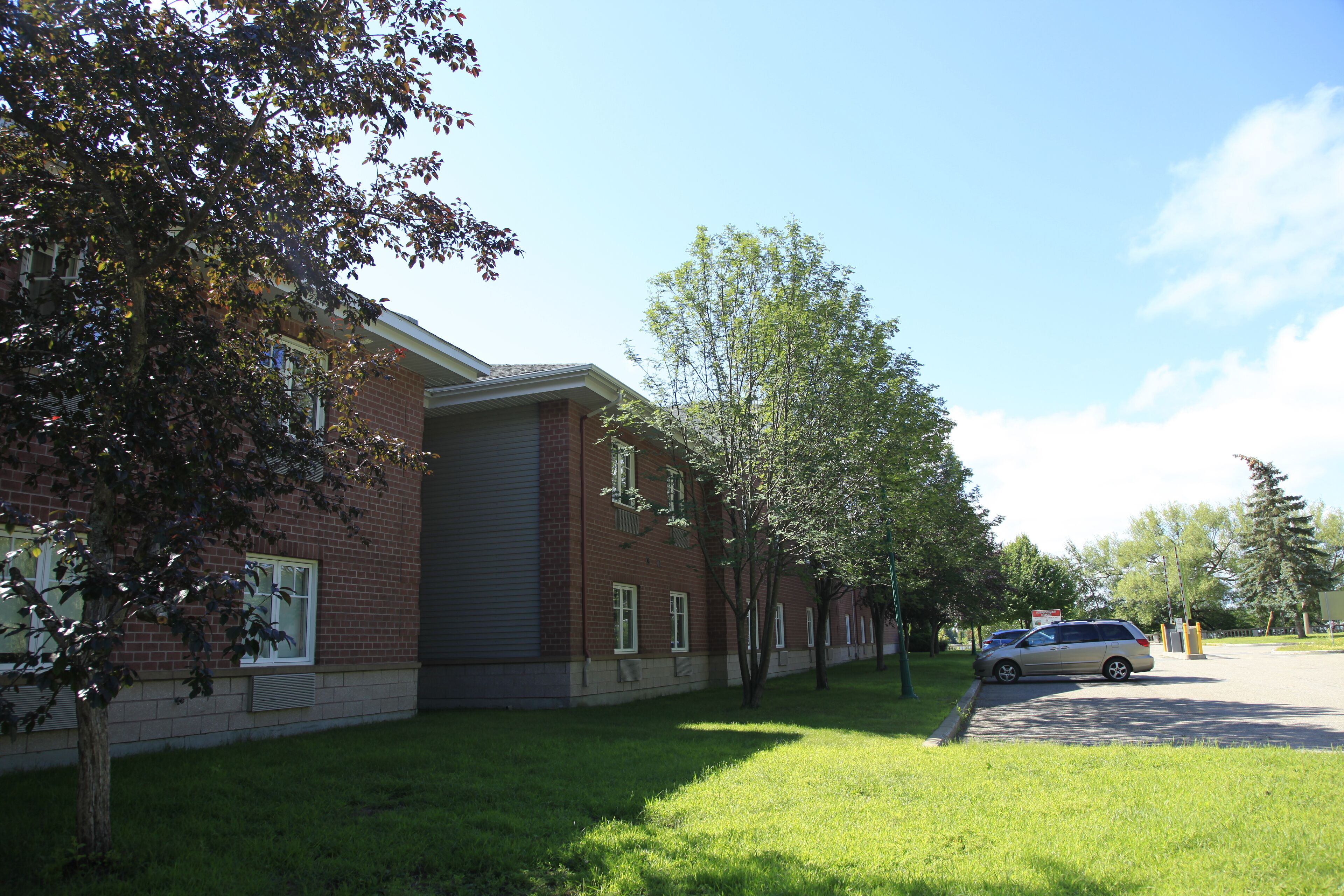 A brick building with a covered parking area and a grassy lawn.