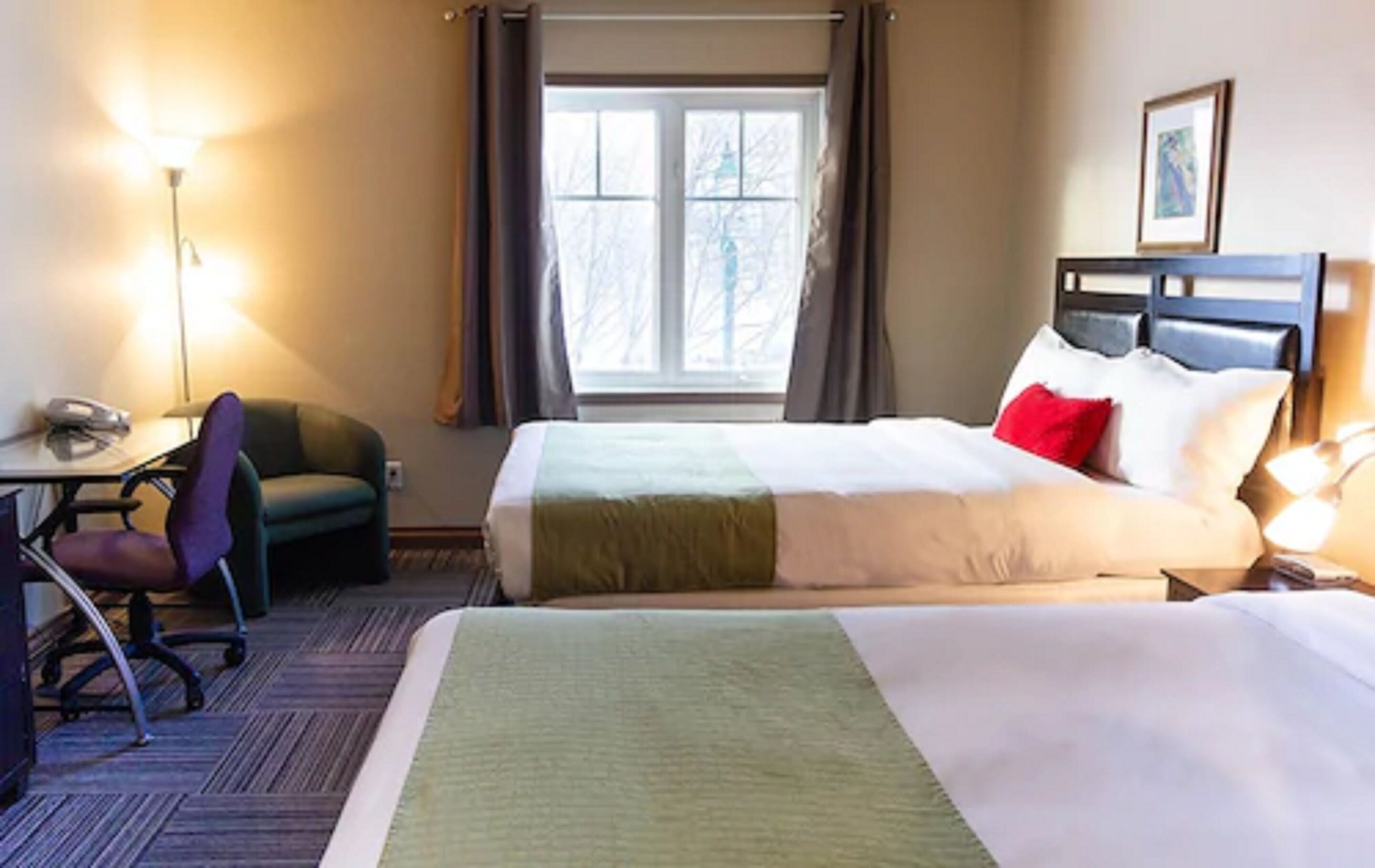 Een hotelkamer met een bed, een bureau, een stoel en een raam met gordijnen.