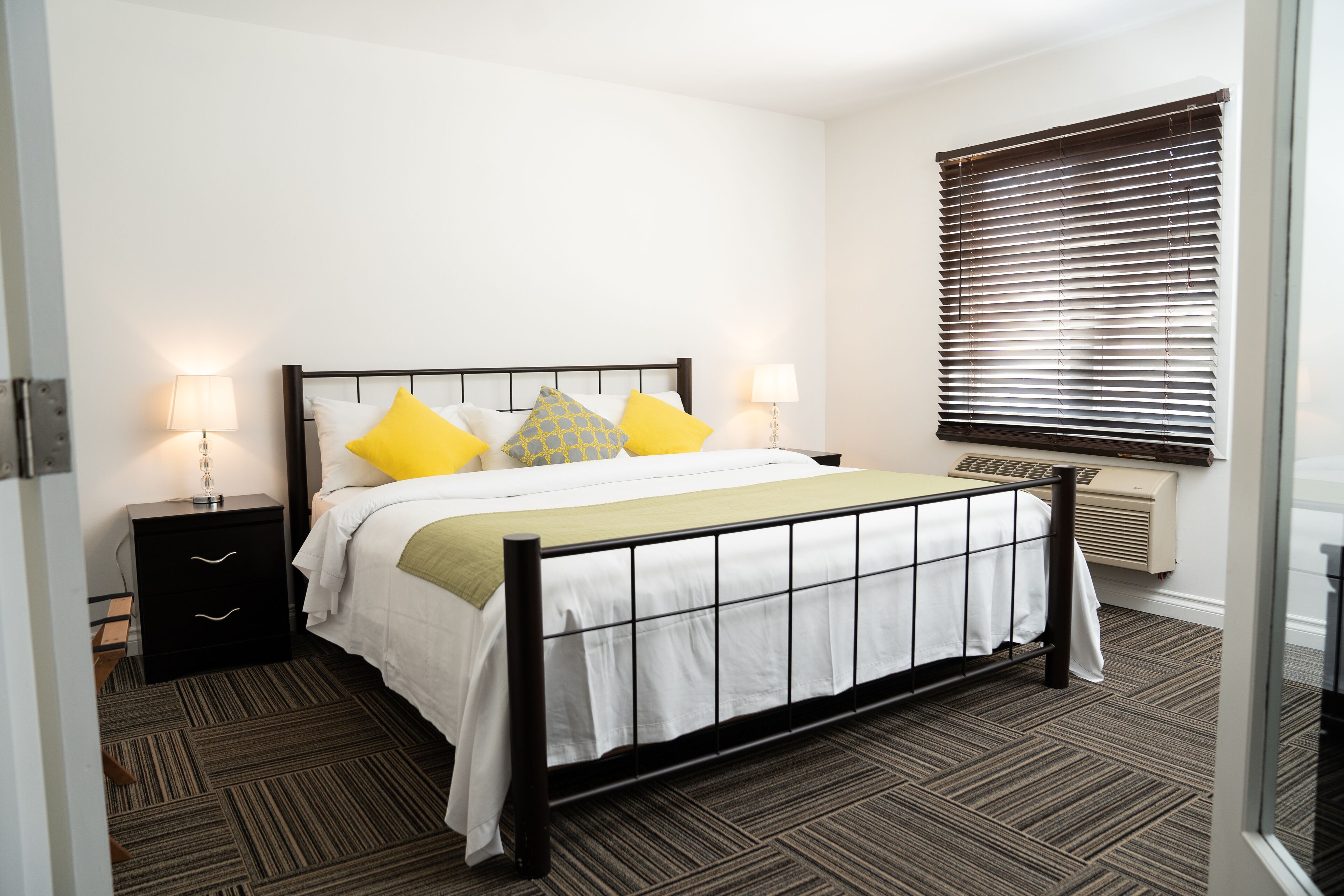 Une chambre à coucher bien rangée, avec un lit, des tables de chevet et une fenêtre équipée de stores.