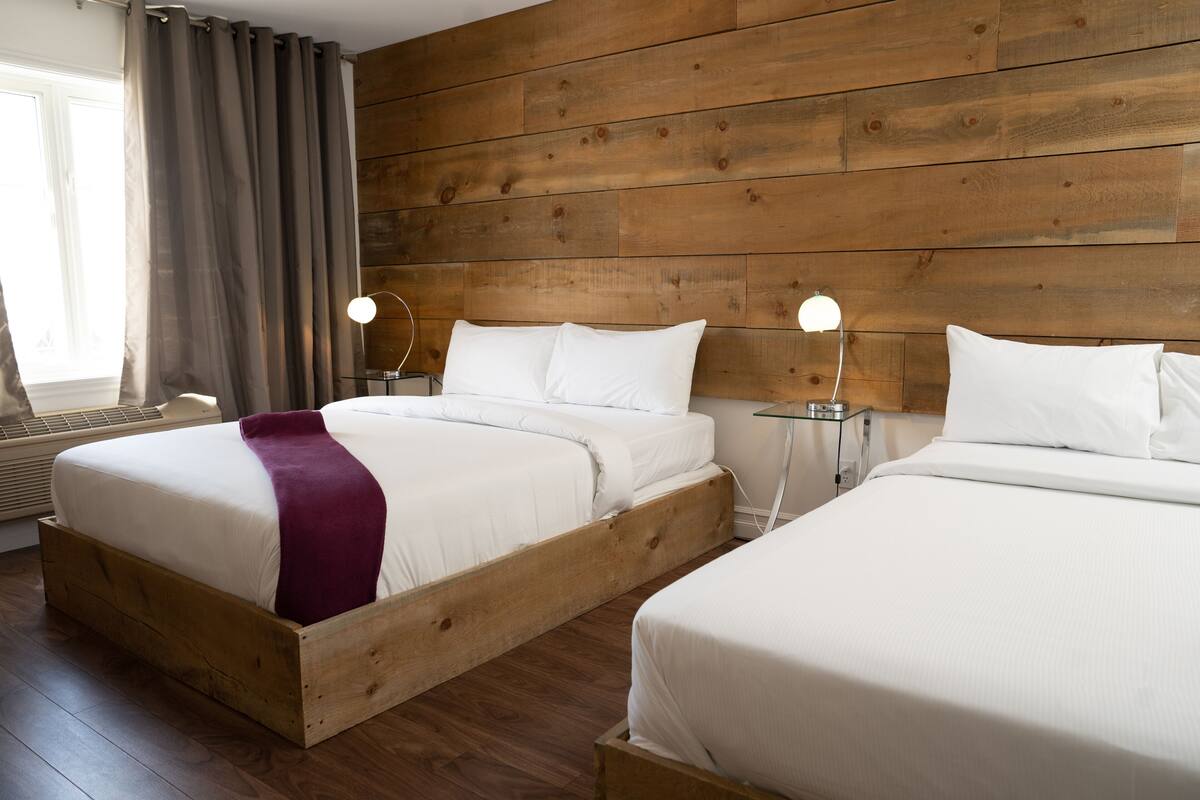 Une chambre d’hôtel avec deux lits en bois, une grande fenêtre avec des rideaux et un mur en bois.