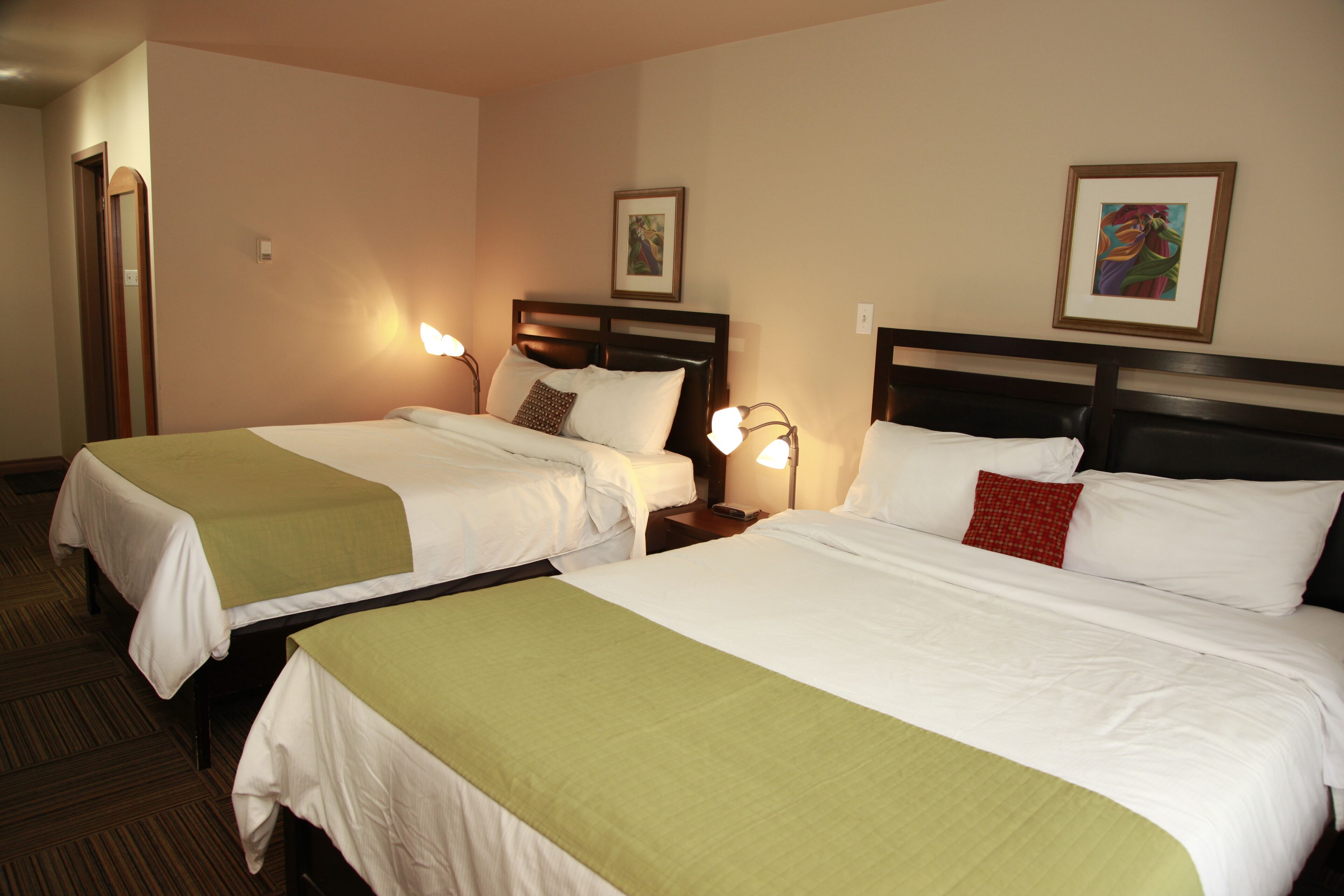 Une chambre d’hôtel avec deux lits, chacun recouvert d’une couvre-lit verte, doté de draps blancs et muni d’une table de chevet avec une lampe.