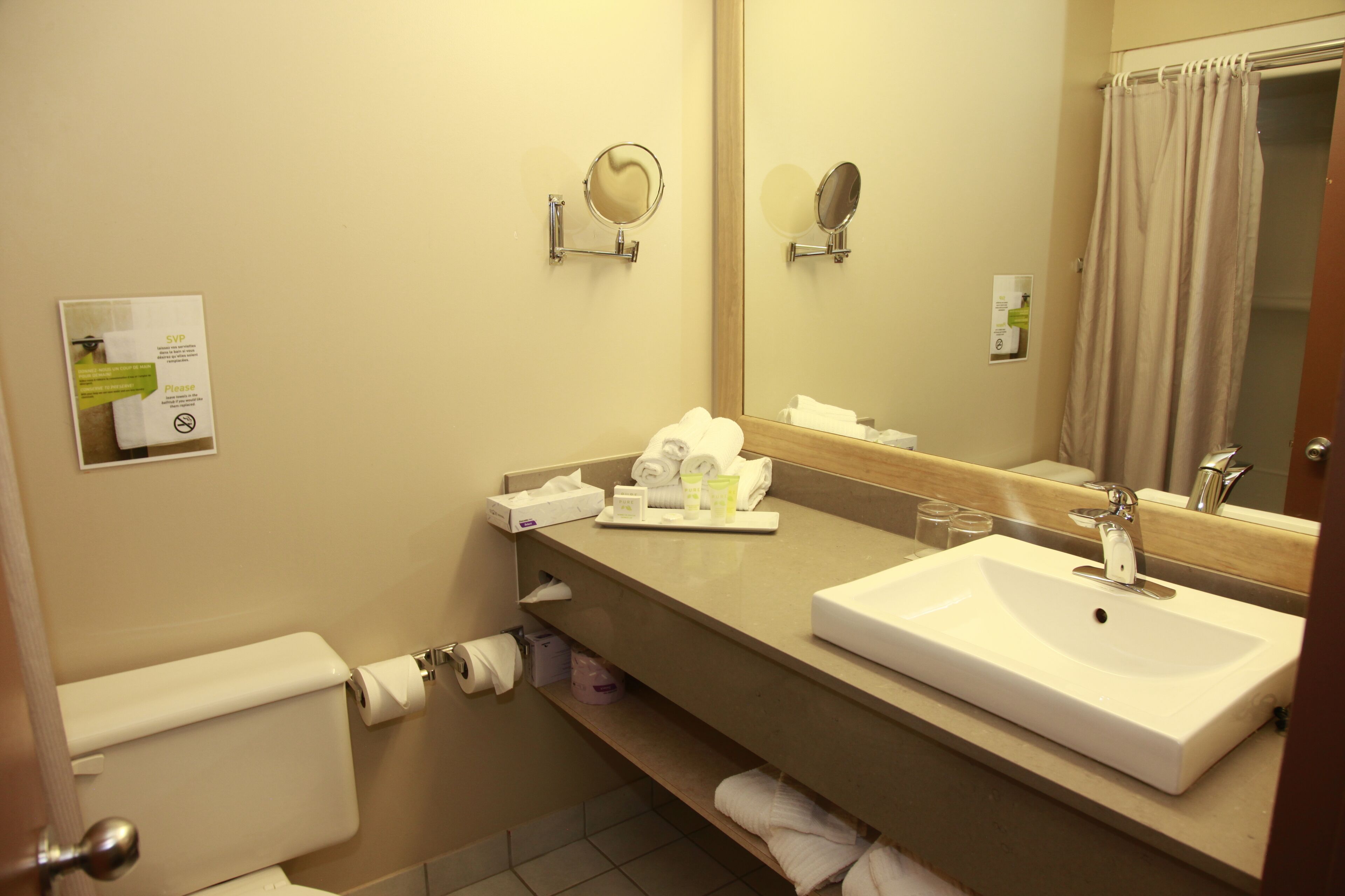 A hotel bathroom with a sink, mirror, towel rack, and toilet.