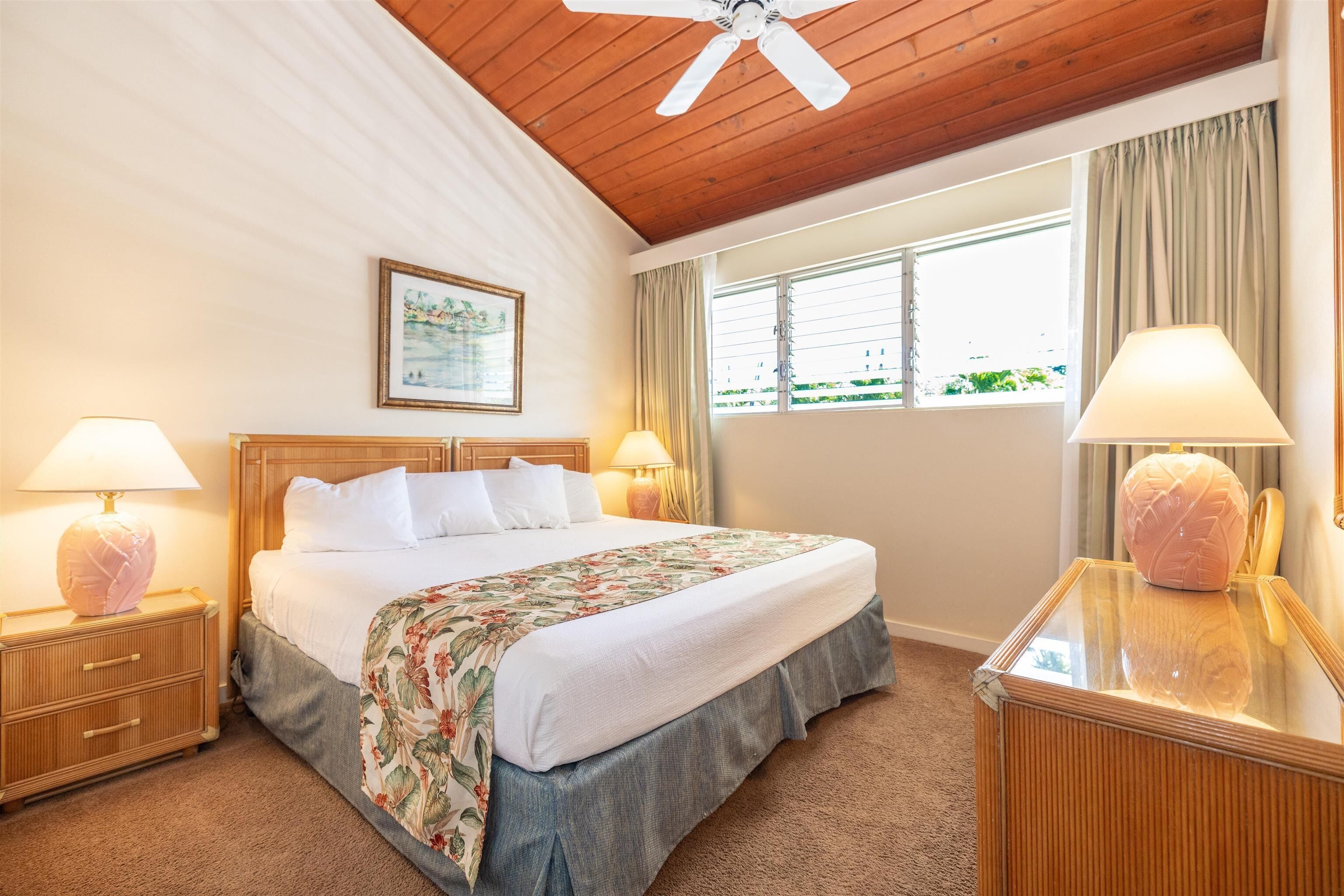 Ein Hotelzimmer mit Holzboden, einem großen Bett mit weißer Bettwäsche, zwei Nachttischlampen, einem Fenster mit Vorhängen und einem gerahmten Bild an der Wand.