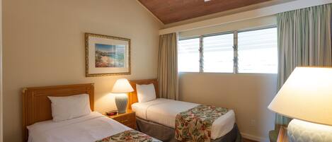 A hotel room with two beds, a ceiling fan, a window with curtains, and a painting on the wall.