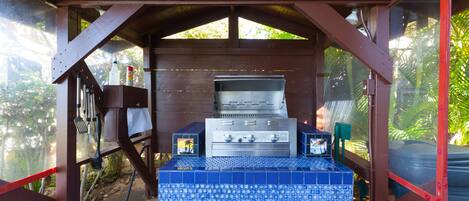 Un espace de cuisson extérieur abrité, équipé d’un barbecue et d’un plan de travail carrelé.