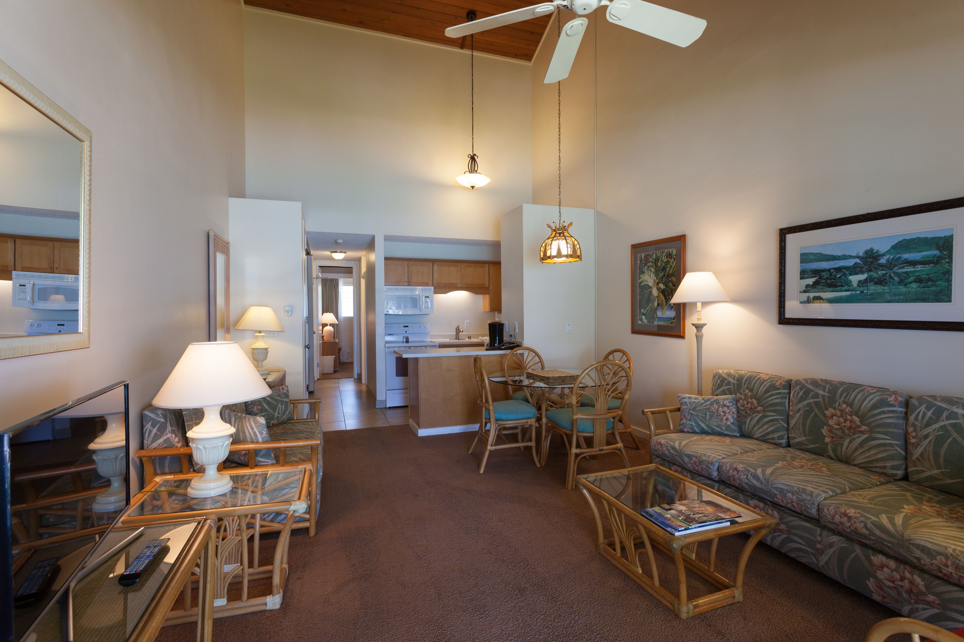 A spacious living room with a sofa, coffee table, and a dining area with chairs. There is a kitchen in the background with a microwave and a refrigerator.