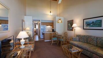 A spacious living room with a sofa, coffee table, and a dining area with chairs. There is a kitchen in the background with a microwave and a refrigerator.