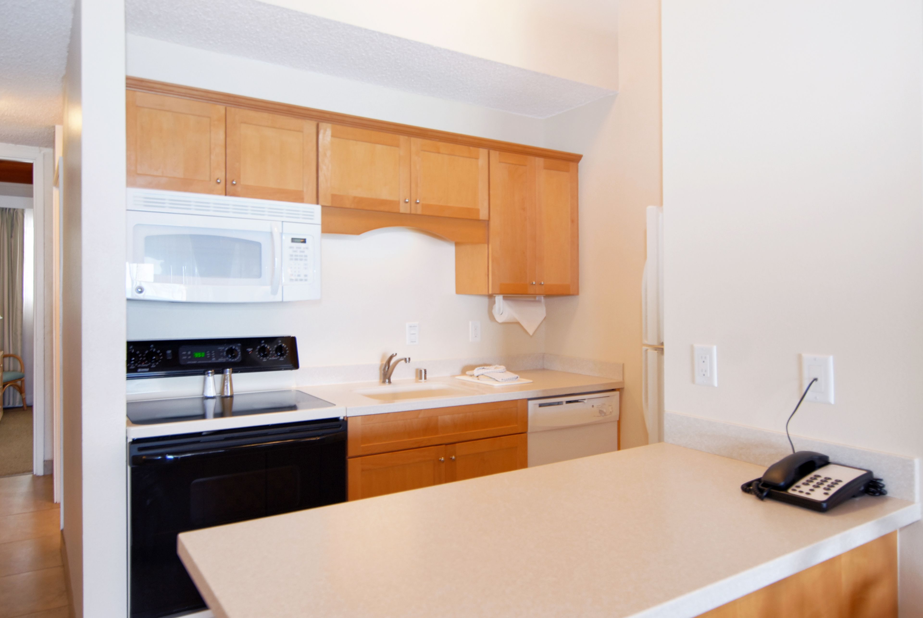 A kitchen with wooden cabinets, a microwave, an oven, a dishwasher, and a telephone on the counter.