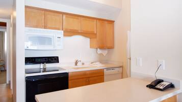 A kitchen with wooden cabinets, a microwave, an oven, a dishwasher, and a telephone on the counter.