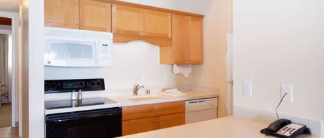A kitchen with wooden cabinets, a microwave, an oven, a dishwasher, and a telephone on the counter.