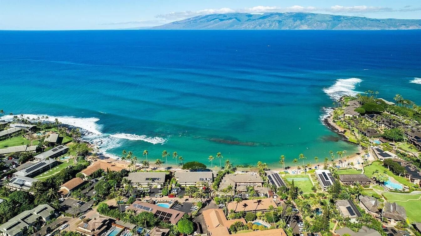 Vista aérea de un complejo turístico costero con vistas al océano, una playa y una montaña al fondo.