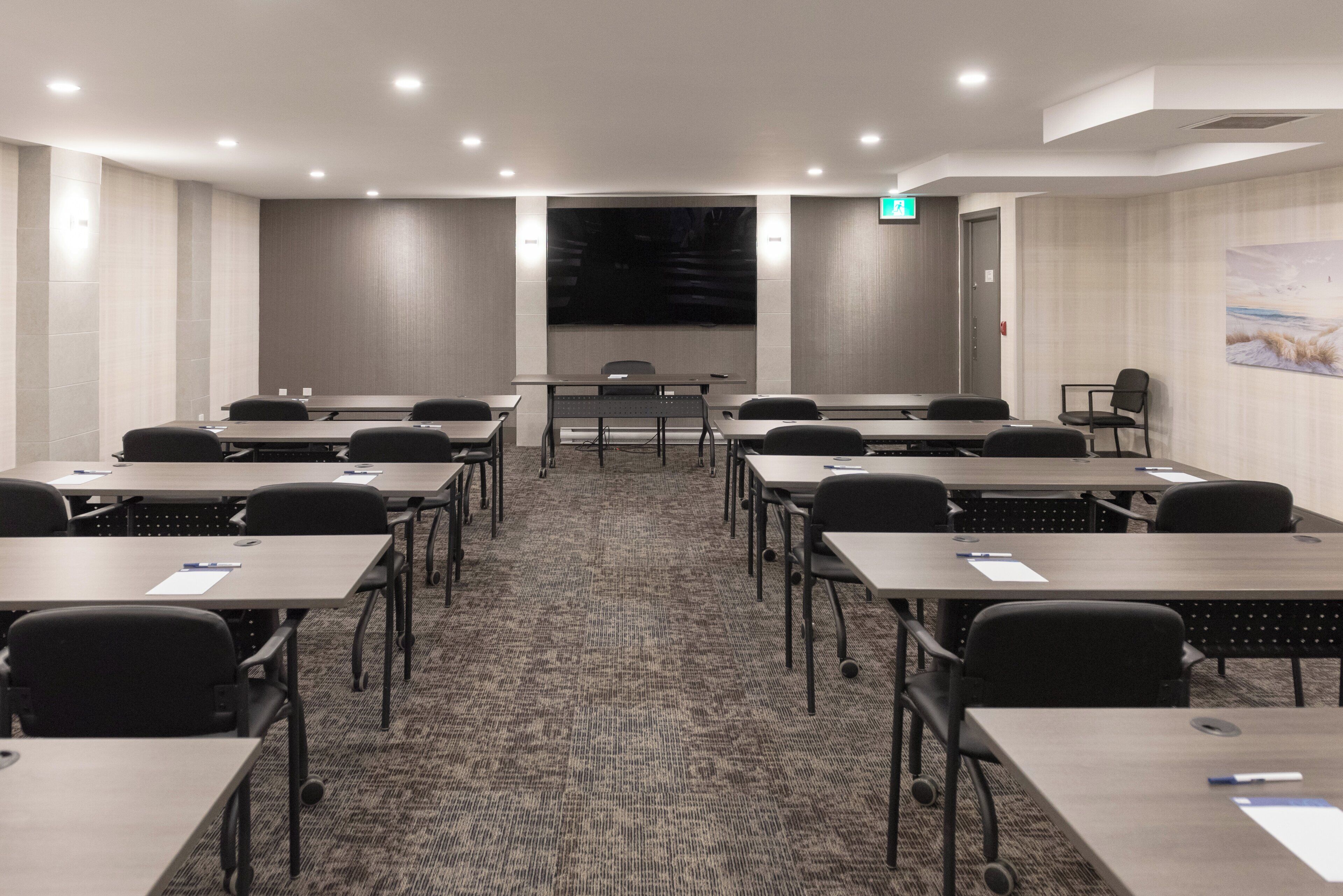 A conference room with multiple tables and chairs, carpeted floor, and recessed lighting.