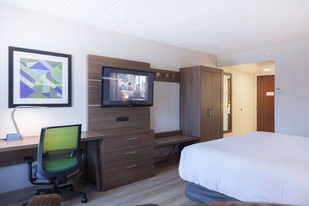 A hotel room with a bed, a desk with a chair, a television, and a wardrobe.