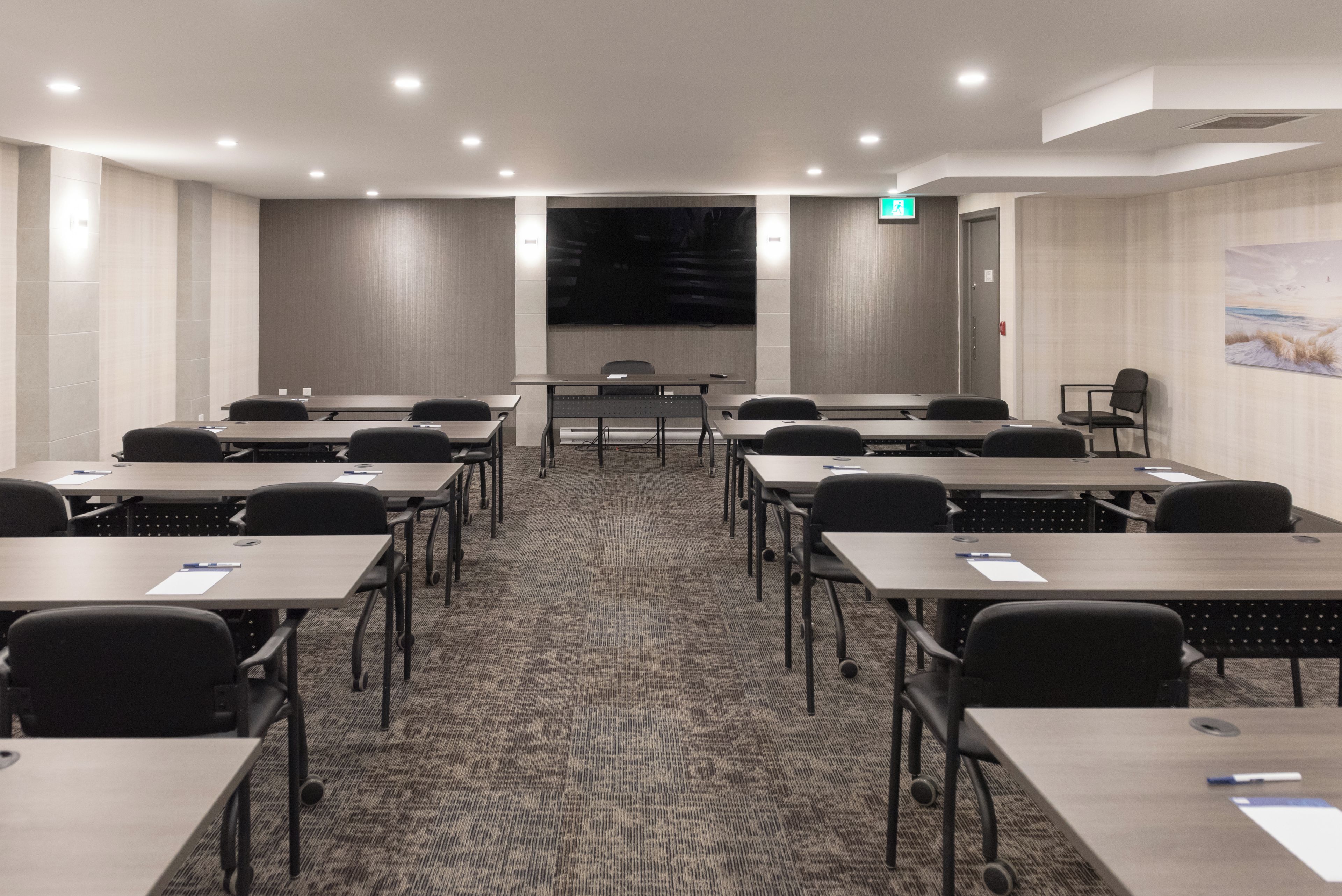 A conference room with multiple tables and chairs, a large screen, and a carpeted floor.