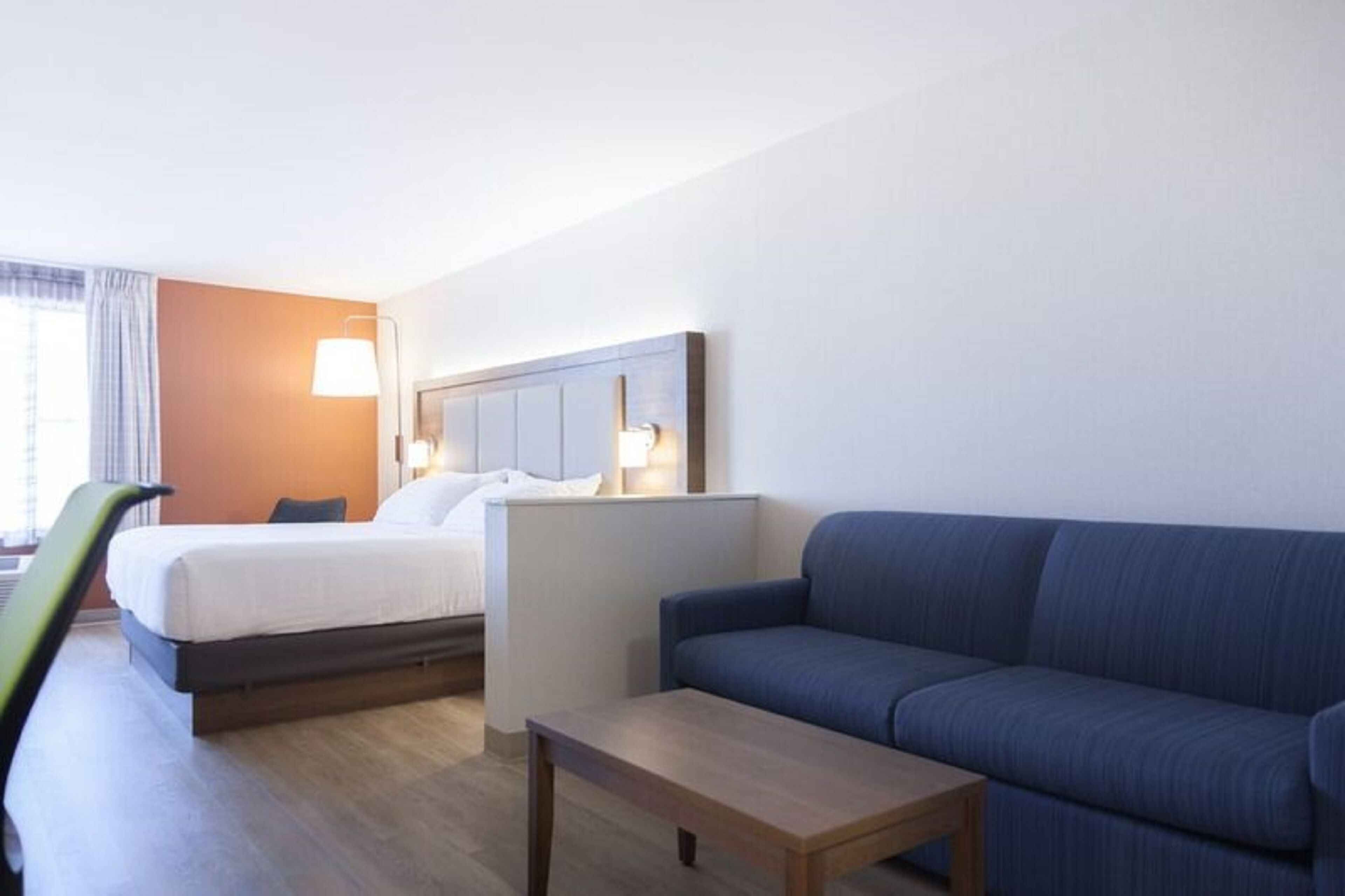Ein Hotelzimmer mit einem Bett, einem blauen Sofa, einem Holztisch und einer Lampe.
