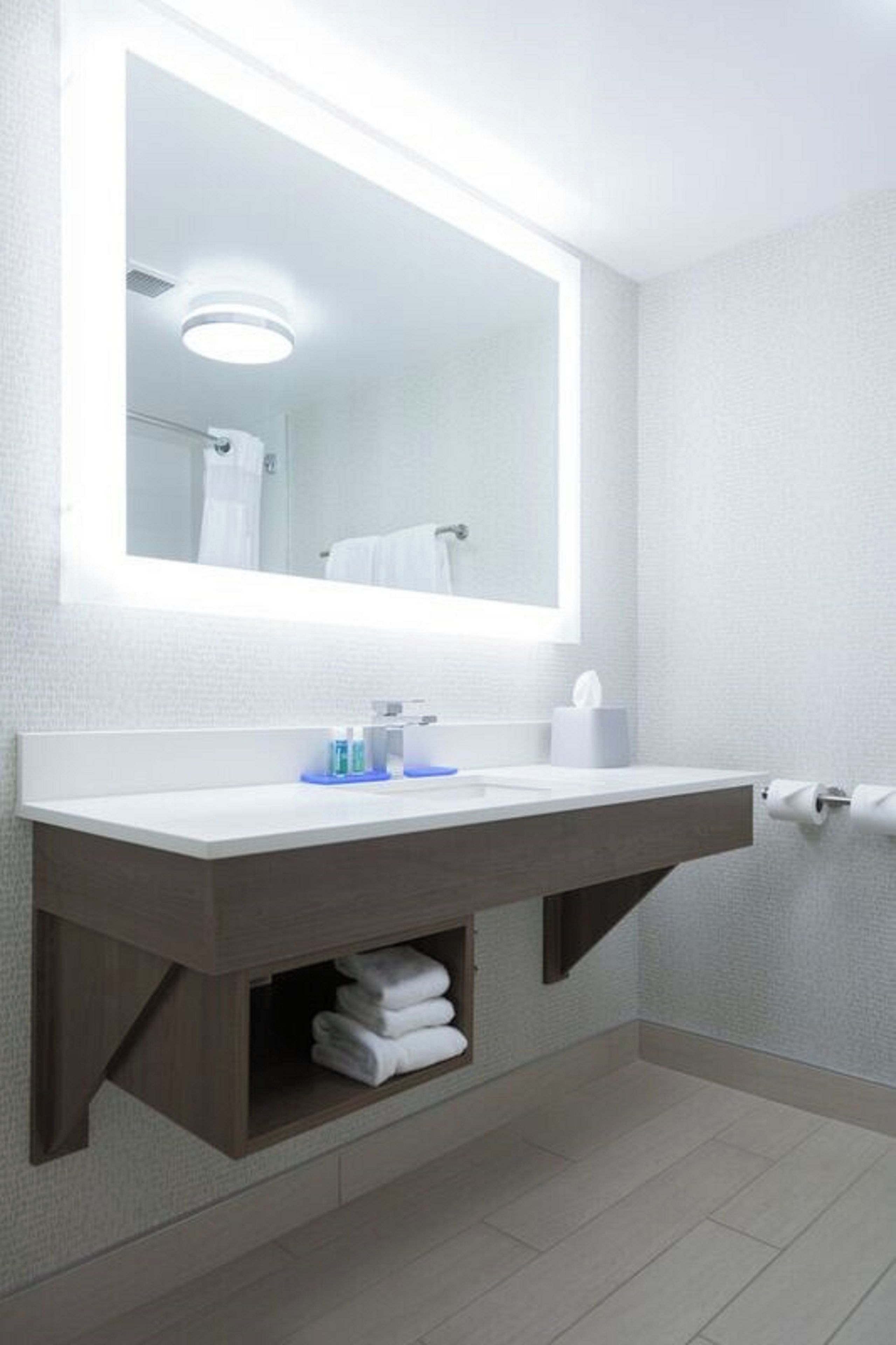 Un baño con un lavabo blanco, un espejo, un perchero para toallas y un dispensador de papel higiénico.