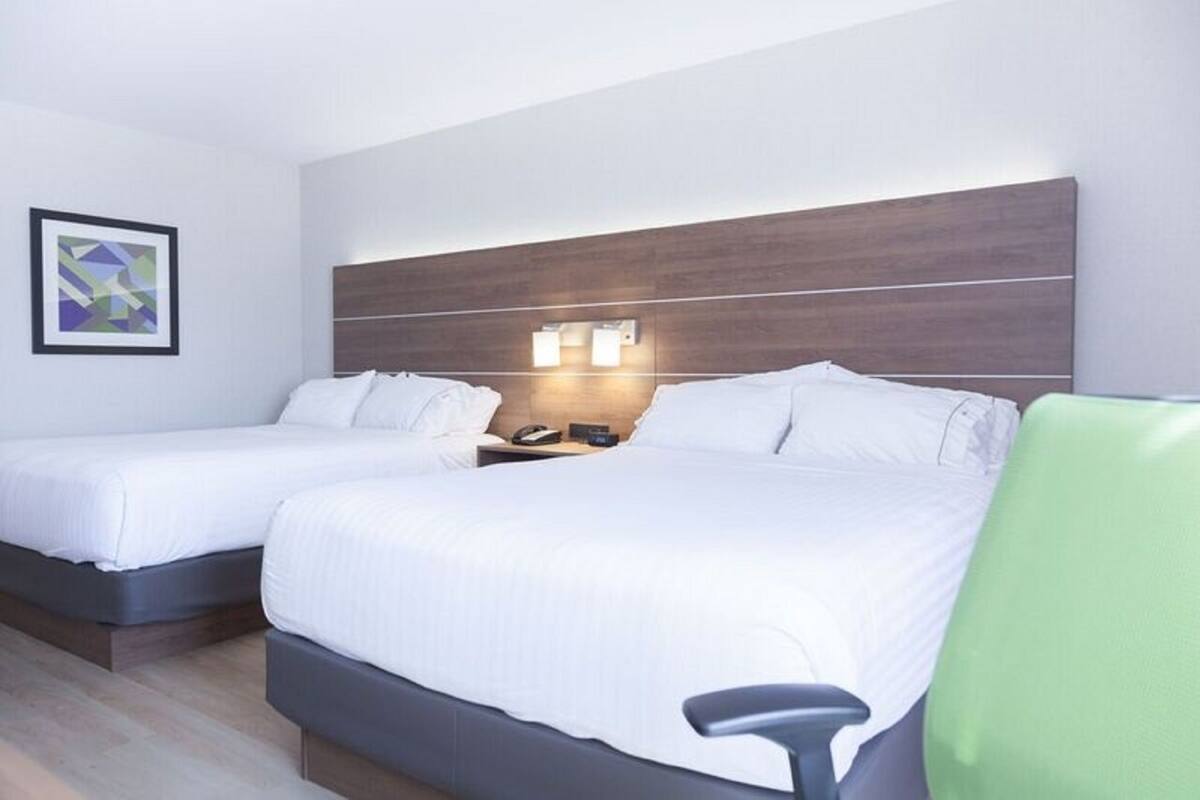 A hotel room with two beds, a wooden headboard, bedside lamps, and a green chair.