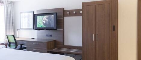 A hotel room with a large bed, a desk with a chair, a television mounted on the wall, and a wardrobe.