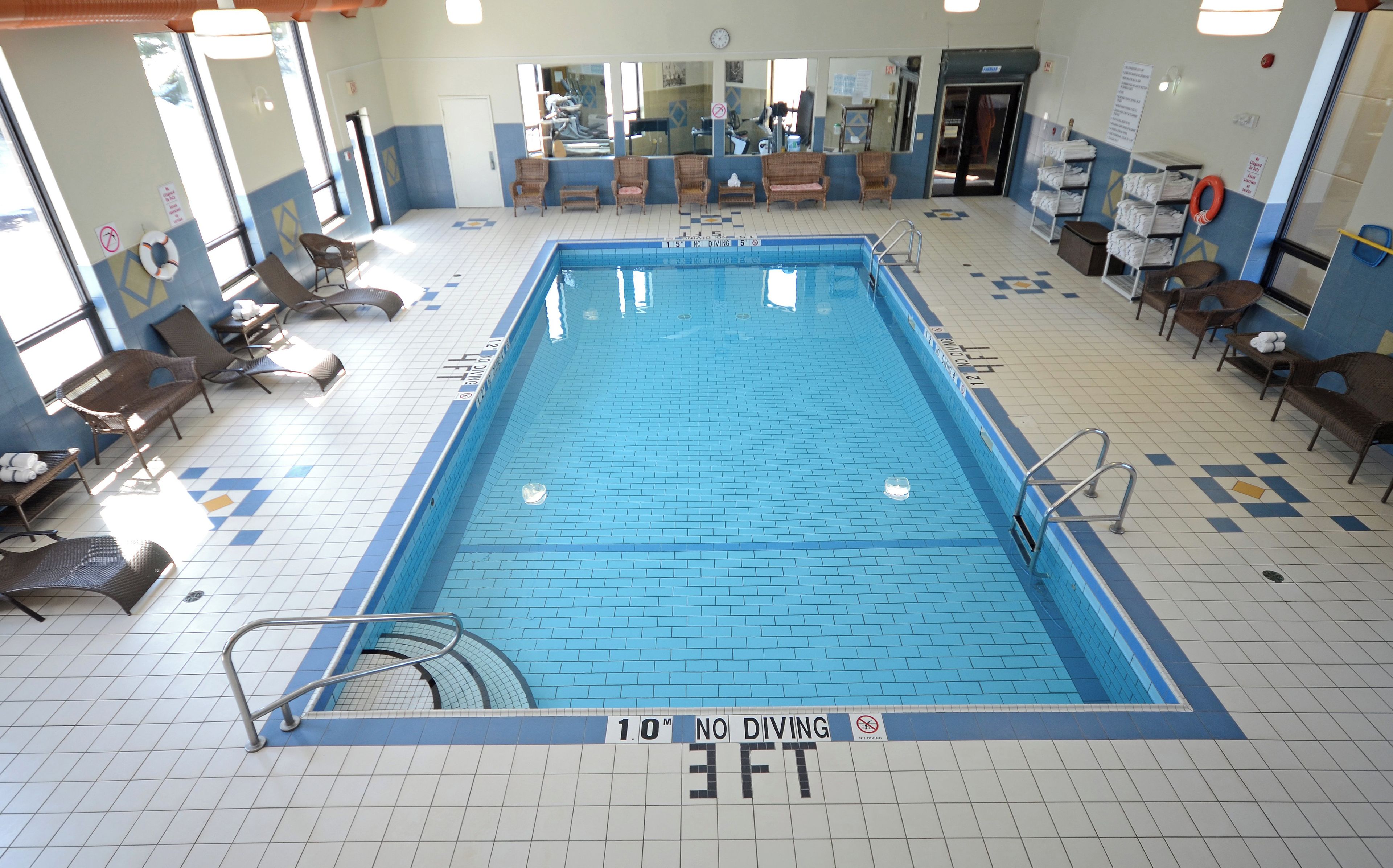 Ein großes Hallenbad mit einem Sprungverbotsschild, Liegestühlen und einem gefliesten Boden.