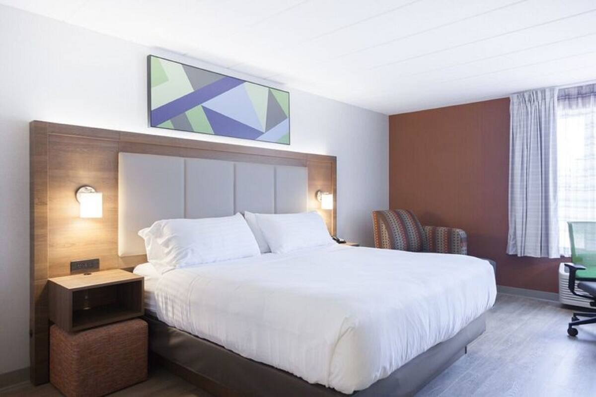 A hotel room with a large bed, a nightstand, a chair, and a painting on the wall.